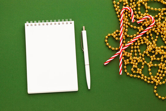 Blank notepad and pen, sweet candy canes and golden garland. Ideas list for holiday gifts or wishes. Notebook for 2021 goals and plans.Happy New Year and Merry Christmas theme. Flat lay, copy space.