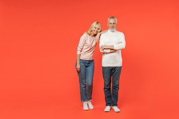Full length of smiling couple two friends elderly gray-haired man blonde woman wearing white pink casual clothes standing looking camera isolated on bright orange color background studio portrait. - obrazy, fototapety, plakaty