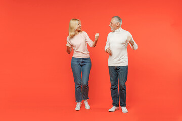 Full length of excited couple two friends elderly gray-haired man blonde woman in white pink casual clothes doing winner gesture clenching fists isolated on orange color background studio portrait.