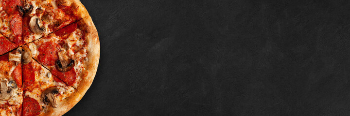 Tasty pizza banner with salame and mushrooms on dark concrete surface with empty space for your text. Top view of sliced pizza. 