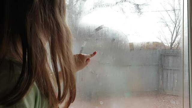 a little girl draws a little man on a fogged window