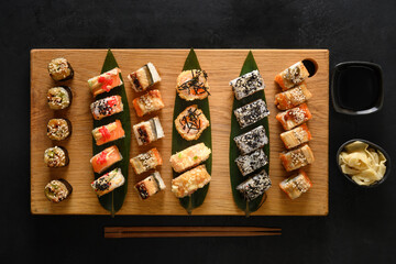 Fototapeta na wymiar Sushi set served on wooden chopping board on black background. View from above. Flat lay style.