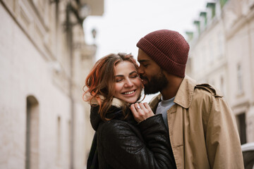 Fototapeta premium Multinational beautiful happy couple smiling and kissing at city street