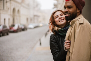 Multinational couple hugging and laughing while walking on city street