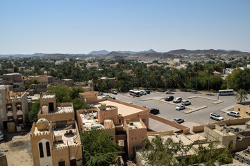 View of a parking lot and some buildings and palm trees that surround Bahla Fort. Bahla, Oman.
