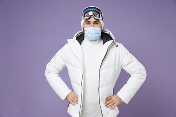 Skier man in warm white windbreaker jacket ski goggles face mask to safe from coronavirus virus covid-19 spend extreme weekend winter in mountains isolated on purple background. People hobby concept.