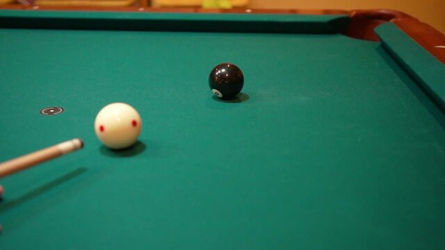 Slow Motion Billiards Person Shooting solid black 8 ball in corner pocket on a pool table with green felt using the cue ball and back spin or draw after practice strokes with cue stick Close Up