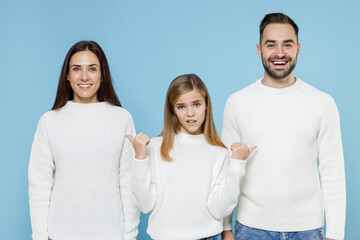 Confused funny child kid daughter teen girl pointing thumbs on young parents mom dad with in casual white sweaters isolated on blue color background studio portrait. Family day parenthood concept.