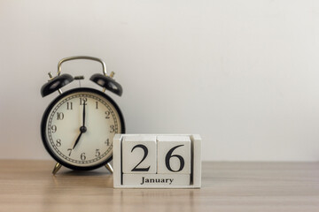 January 26 on a white calendar, next to a retro alarm clock on a light background.Calendar for January.Copy of the space.