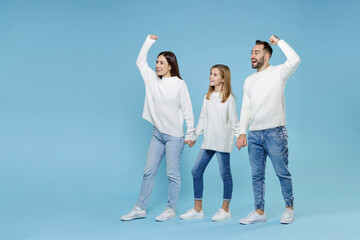 Fototapeta premium Full length of excited young parents mom dad with child kid daughter teen girl in sweaters holding hands clenching fists isolated on blue background studio portrait. Family day parenthood concept.