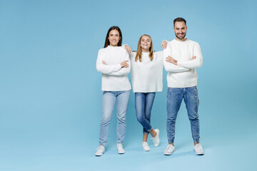 Fototapeta premium Full length of funny young happy parents mom dad with child kid daughter teen girl in white sweaters holding hands crossed isolated on blue background studio portrait. Family day parenthood concept.