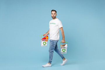 Full length of serious young man in volunteer t-shirt hold baskets with plastic paper trash isolated on blue background studio portrait. Voluntary free assistance help trash sorting recycling concept.
