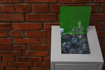 Many used plastic bottles in metal bin near brick wall, space for text. Recycling problem