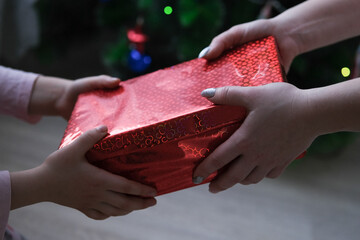 women's and children's hands hold a red gift box on a background of colorful bokeh.
