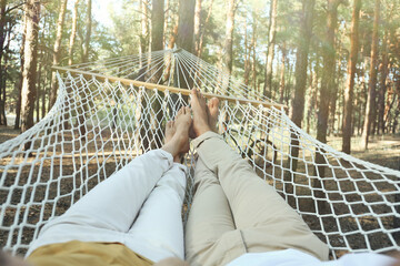 Couple resting in hammock outdoors on summer day, closeup of legs