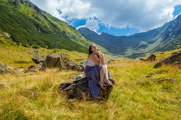 Foto op Canvas Sensual pretty girl in long blue white dress sits on a rock and dreaming against the high mountains backgdrop. Woman sitting near Transfegerasan, one of the most spectacular mountain road in the world © pijav4uk