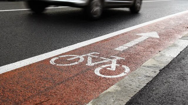 Asphalt bicycle path in a town, while cars drive by. Low angle.