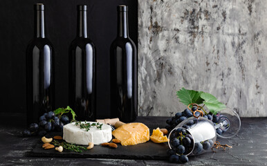 Wine bottles cheese nuts and grapes on slate board. Wine bar snacks. Wine composition on dark...
