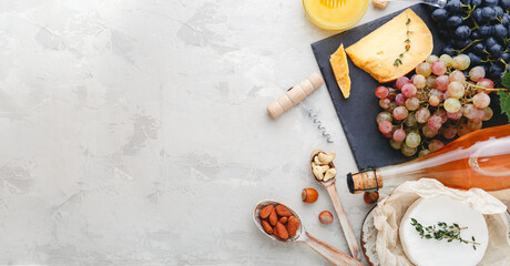 Rose wine bottle cheese nuts and pink and black grapes, honey. Camembert cheese, wine bar snacks. Wine composition on light gray rustic concrete background. Long web banner with copy space.