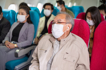 Asian passengers wearing medical face mask sitting on seat in the airplane cabin. travel on holiday, vacation or work abroad during Coronavirus epidemic. new normal lifestyle and social distancing