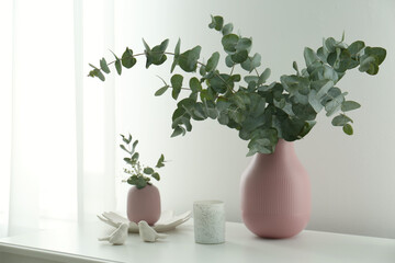 Beautiful eucalyptus branches, candle and bird figures on white table indoors. Interior element