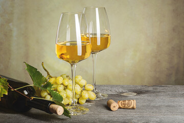 White wine in glasses, wine bottle and grapes on an old wooden table.