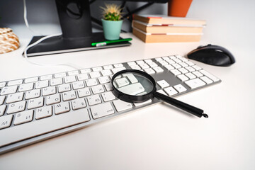 A glass magnifier lies next to the keyboard in a cozy workplace. The concept of Internet search