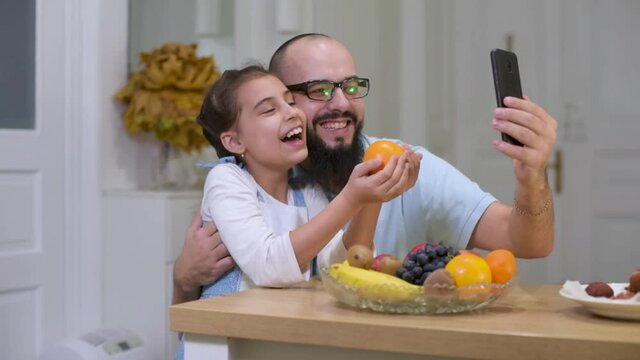 Father and daughter take a picture of fruit in the kitchen. Happy young father with cute daughter in the kitchen. Food for children.