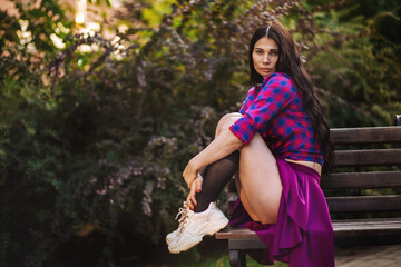 A girl in a black dress white sneakers and knee socks is sitting on a bench