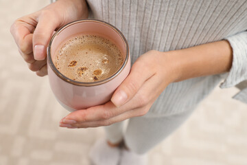 Woman holding cup of coffee indoors, closeup