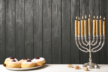 Silver menorah near sufganiyot and dreidels with symbols Nun, He, Pe, Gimel on grey wooden background. Space for text