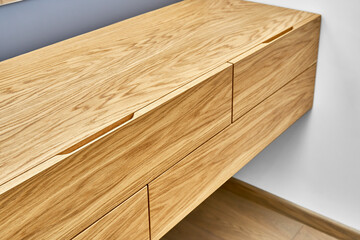 Stylish floating cabinet of light brown natural timber and finger pull design in contemporary apartment interior design closeup