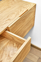 Stylish floating cabinet of natural wood with opened empty drawer near white wall in contemporary apartment interior design closeup