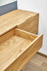 Stylish floating cabinet of natural wood with opened empty drawer near white wall in contemporary apartment interior design closeup