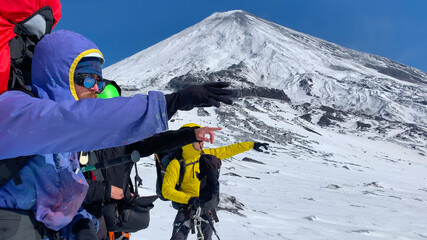 Three mountaineers-travelers stand at the foot of the Klyuchevskaya volcano.