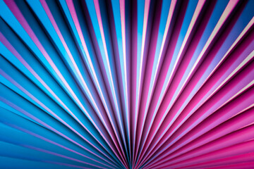 Fototapeta premium Fan made of paper or cardboard close-up. A three-dimensional object. Three-dimensional blue-pink background. Abstract geometric background. Partly blurry image of a paper object.