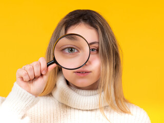Girl holds a magnifying glass in front of her eye and looks at camera. Observant young woman with magnifying glass. Exploring what's around us. Detailed review of interesting object.