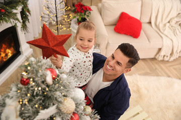 Father and little daughter decorating Christmas tree with star topper in room, above view