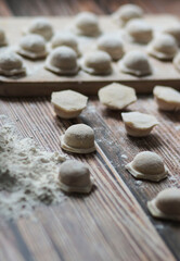 Fototapeta na wymiar Cooking dumplings. Raw dumplings lie on a wooden board. Nearby lies flour, rolling pin and dough against a background of wood.