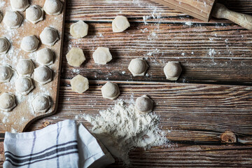
Cooking dumplings. Raw dumplings lie on a wooden board. Nearby lies flour, rolling pin and dough against a background of wood.