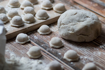 Fototapeta na wymiar Cooking dumplings. Raw dumplings lie on a wooden board. Nearby lies flour, rolling pin and dough against a background of wood.