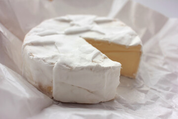 Camembert cheese on white packaging paper. Top view. Close up of white cheese