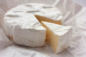 Camembert cheese on white packaging paper. Top view. Close up of white cheese