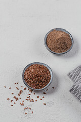 Brown flax seed and ground or crushed flaxseed or linseed in small bowl on a light gray background.
