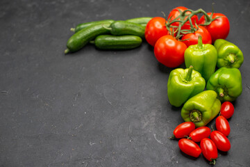 Fresh vegetables red tomatoes with stems green peppers and cucumbers necessary for cooking on dark background