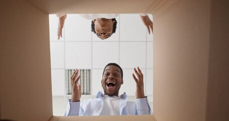 Afro american couple man and young black woman look inside cardboard box parcels unpack delivery order take out gift box rejoice presents for Christmas birthday holiday celebration concept bottom view
