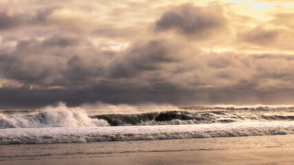 Rough surf under dark ominous storm clouds, with spray coming off large waves breaking. 