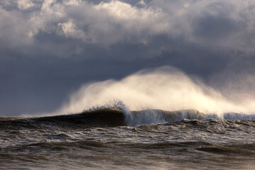 Rough surf under dark ominous storm clouds, with spray coming off large waves breaking. 