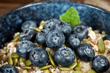 Oatmeal porridge with blueberries and pumpkin and chia seeds in a blue ceramic bowl on a wooden background. Trendy healthy eating concept.