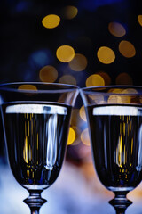 Glasses with sparkling champagne and golden bokeh on a dark background. Atmsofer of magic and celebration.